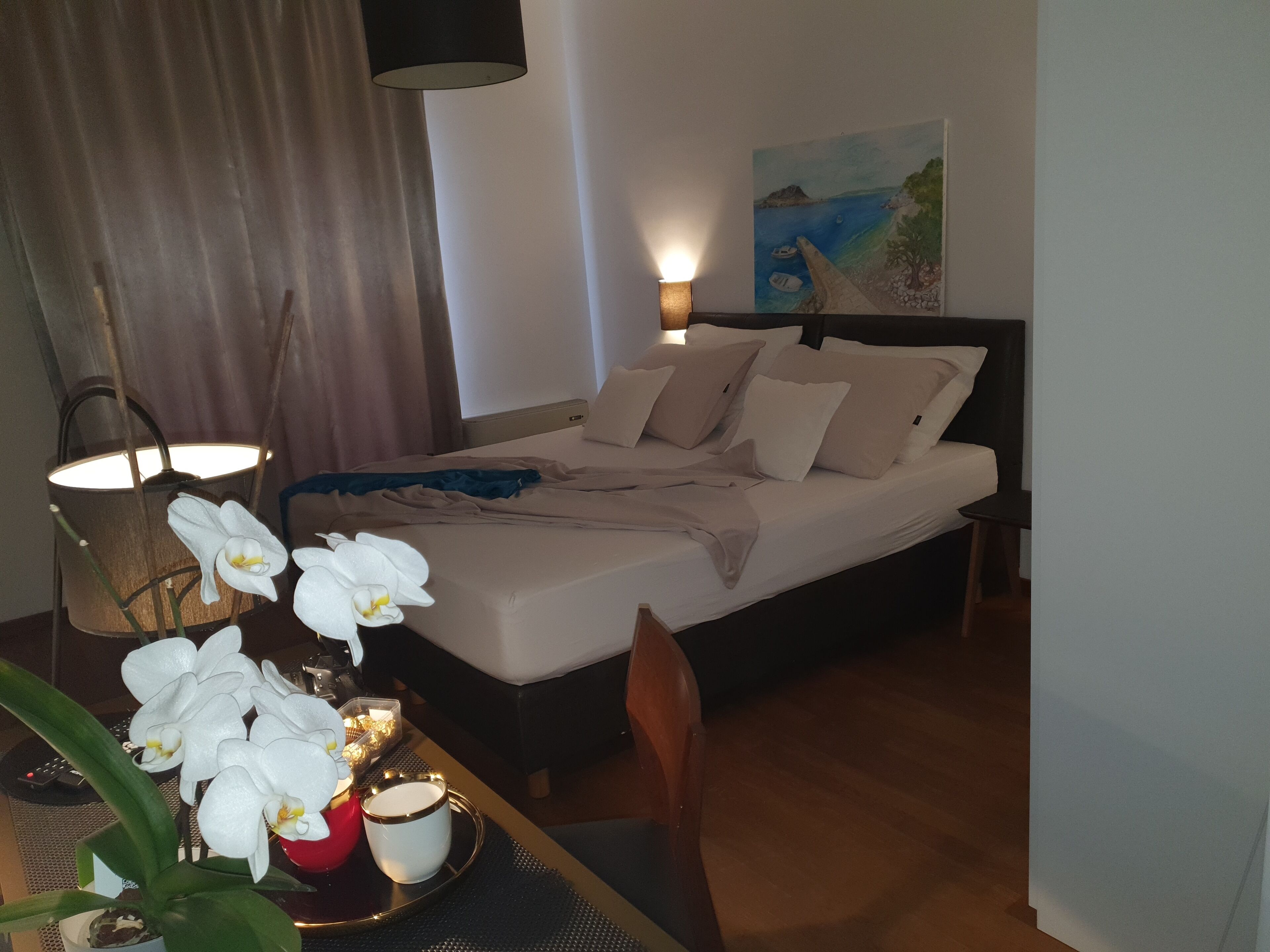 Habitación de hotel impecable con una cama, una mesita con flores y un cuadro en la pared.