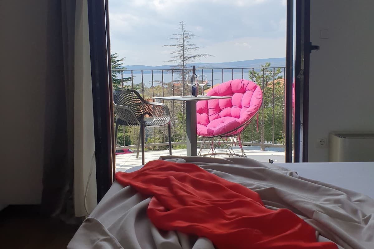 A bedroom with a bed, a balcony with a chair, and a view of the outdoors.
