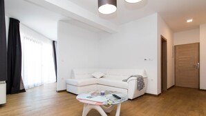 A modern living room with a white sofa, a glass coffee table, and wooden flooring. - Pansion Preza (Crikvenica)