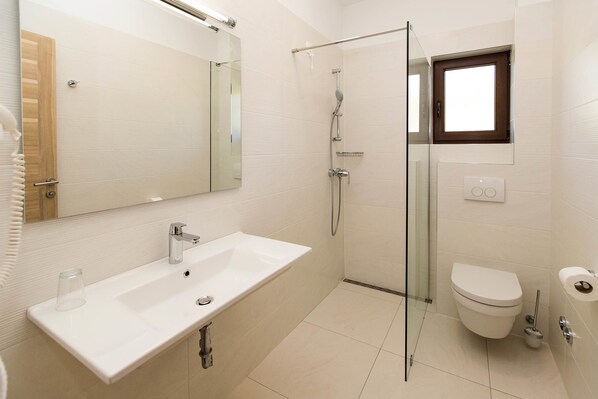 Un baño moderno con ducha de vidrio, lavamanos blanco y retrete.