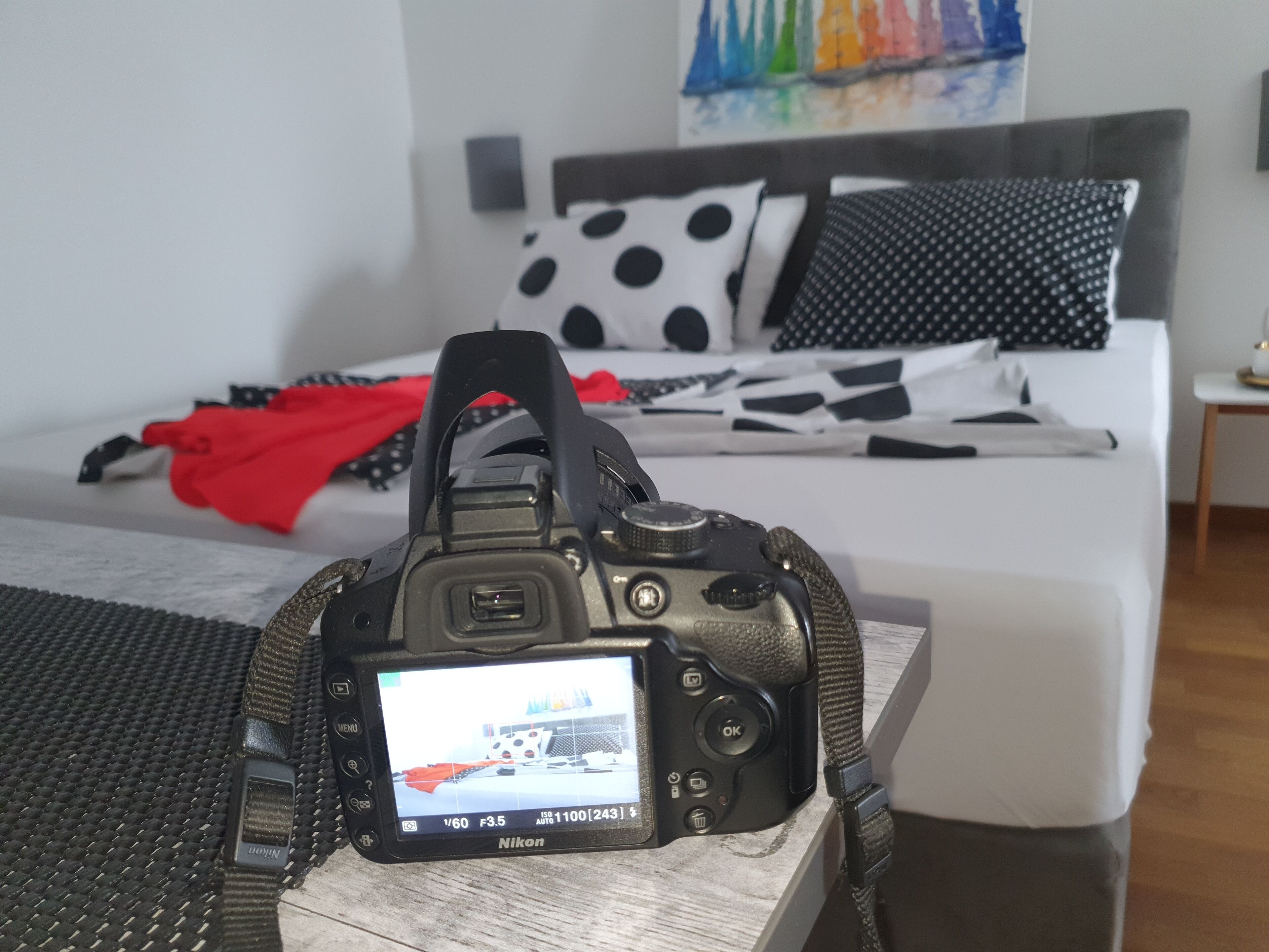 A camera on a wooden surface with a bed in the background.
