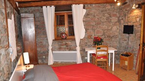 Ein Schlafzimmer mit Steinwand, einem hölzernen Bett, einem Schreibtisch mit Stuhl und einem an der Wand montierten Fernseher.