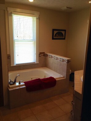 A bathroom with a bathtub, a window with blinds, a framed picture on the wall, and a red towel on the tub.