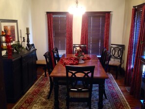 A dining room with a wooden table, six chairs, red curtains, and a chandelier.