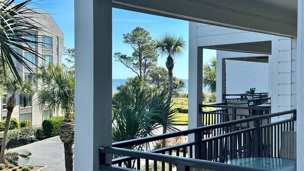 A balcony with a view of the ocean, palm trees, and a building with large windows. - Elegance at the beach -Ocean View Villa, Gorgeous! (Hilton Head Island)