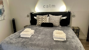A neatly made bed with a grey textured bedspread, two folded towels, and a headboard with a 'calm' sign. - Elegance at the beach -Ocean View Villa, Gorgeous! (Hilton Head Island)