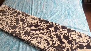 Uma cama com colcha azul e branca estampada, um cobertor marrom e branco e duas almofadas com padrão azul e branco.