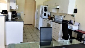 Een moderne keuken met witte apparaten, een glazen eettafel en een laptop op het aanrecht.