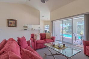 Un saló amb una taula de café de vidre, sofàs vermells i vistes a una piscina a través de grans portes corredisses de vidre.