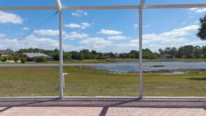 A covered outdoor area with a view of a lake and houses in the background. - Maria Maria | Lake View Home with Heated Pool (Lehigh Acres)