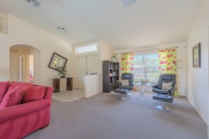 A living room with a red sofa, two leather chairs, a bookshelf, and a window with floral curtains. - Maria Maria | Lake View Home with Heated Pool (Lehigh Acres)