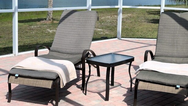 Een overdekt terras met twee comfortabele stoelen en een kleine tafel, met uitzicht op een meer en groen.