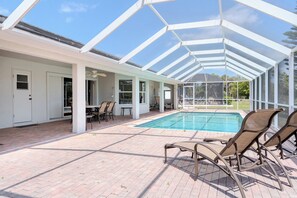 A covered outdoor swimming pool area with chairs and a table, surrounded by a glass enclosure. - Maria Maria | Lake View Home with Heated Pool (Lehigh Acres)