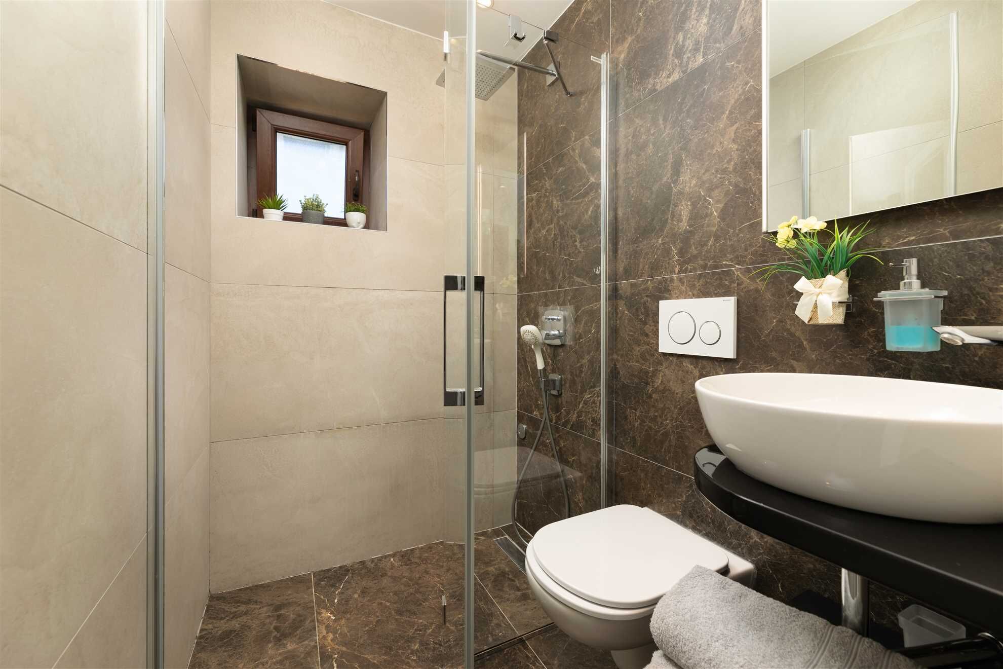 Ein modernes Badezimmer mit einer gläsernen Duschkabine, einem weißen Waschbecken und einer Toilette.