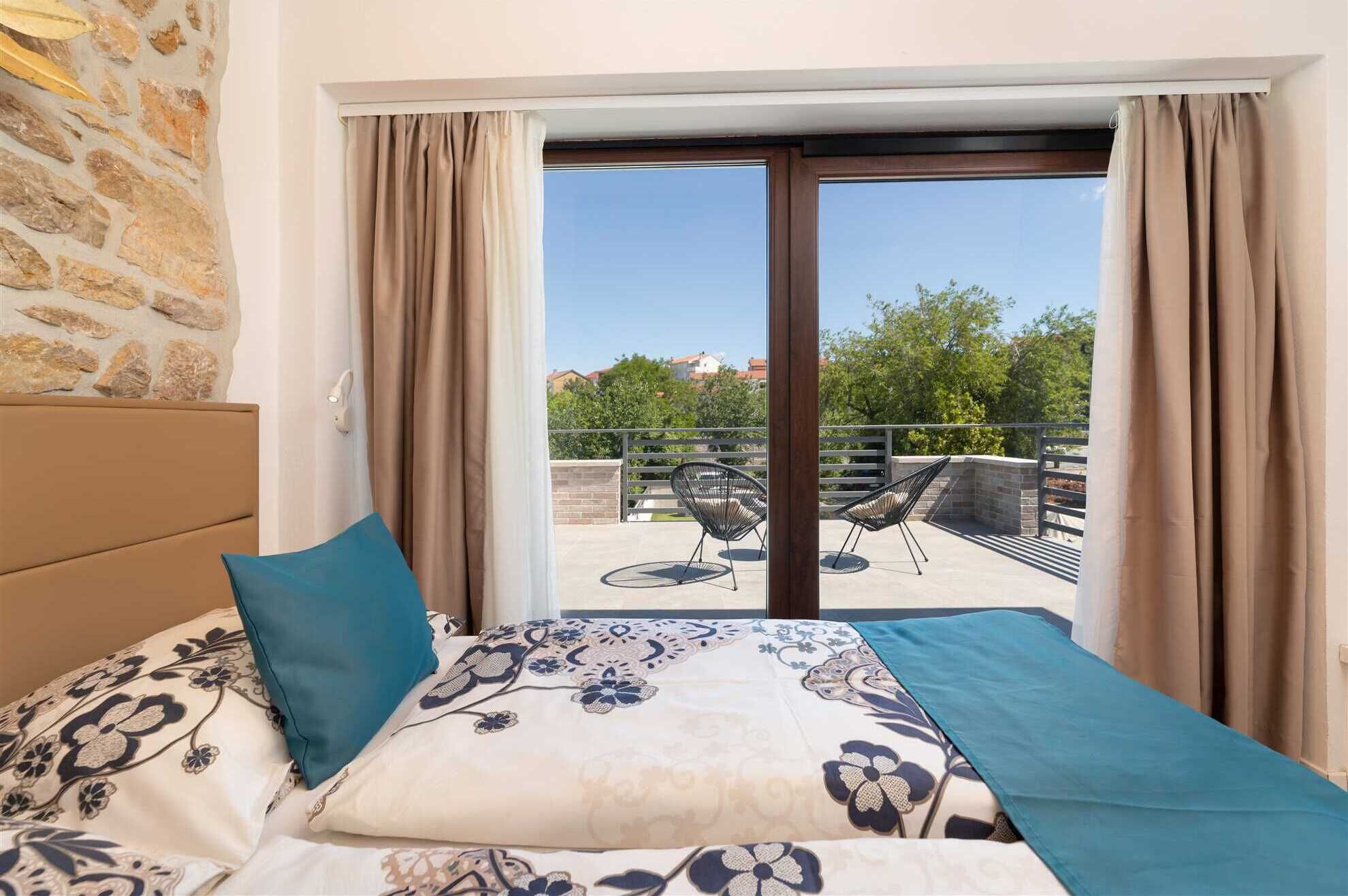 A bedroom with a bed, a view of an outdoor seating area, and a stone wall.