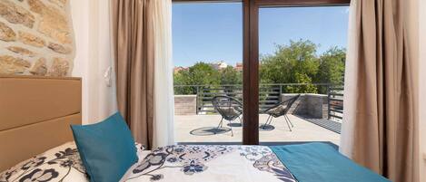 A bedroom with a bed, a view of an outdoor seating area, and a stone wall.