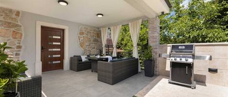 An outdoor patio with a stone wall, a grill, and a seating area with a sofa and cushions.