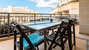 Een balkon met een glazen tafel en stoelen, uitzicht op een stadsbeeld, en een gebouw met balkon.