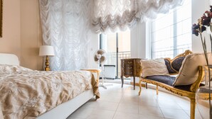 Ruime slaapkamer met een groot bed, een zithoek met een bank en fauteuils, een kleine tafel en een decoratieve ventilator.