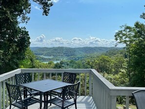 Eine Terrasse mit Tisch und Stühlen mit Blick auf einen See und bewaldete Hügel.