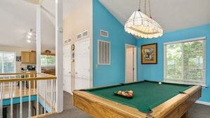 A pool table in a room with blue walls, a wooden ceiling, and a staircase.