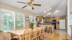 A dining area with a wooden table and chairs, a ceiling fan, and a kitchen in the background.