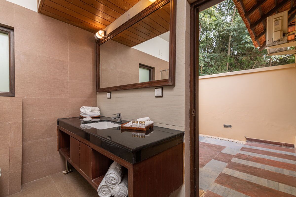 Un baño con techo de madera, un espejo grande, un lavamanos negro y un perchero para toallas.
