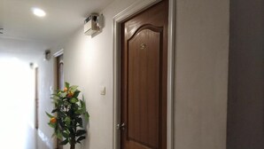 A hallway with a wooden door, a potted plant, and a wall-mounted air conditioning unit. - Aum Hotel (Puttaparti)