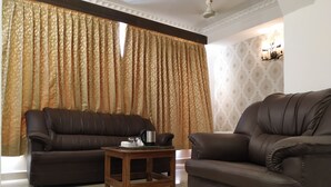 A living room with two brown leather sofas, a wooden coffee table, and a patterned curtain. - Aum Hotel (Puttaparti)