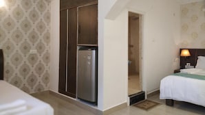 A hotel room with a bed, a nightstand, a wall-mounted lamp, a wardrobe, and a door leading to a bathroom. - Aum Hotel (Puttaparti)