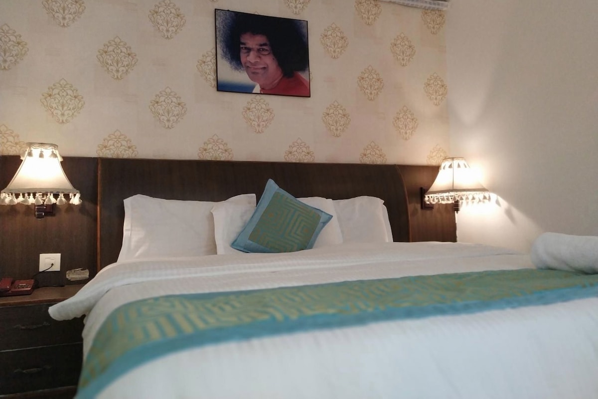 A hotel room with a bed, two bedside lamps, a wall-mounted air conditioner, and a decorative wall pattern.
