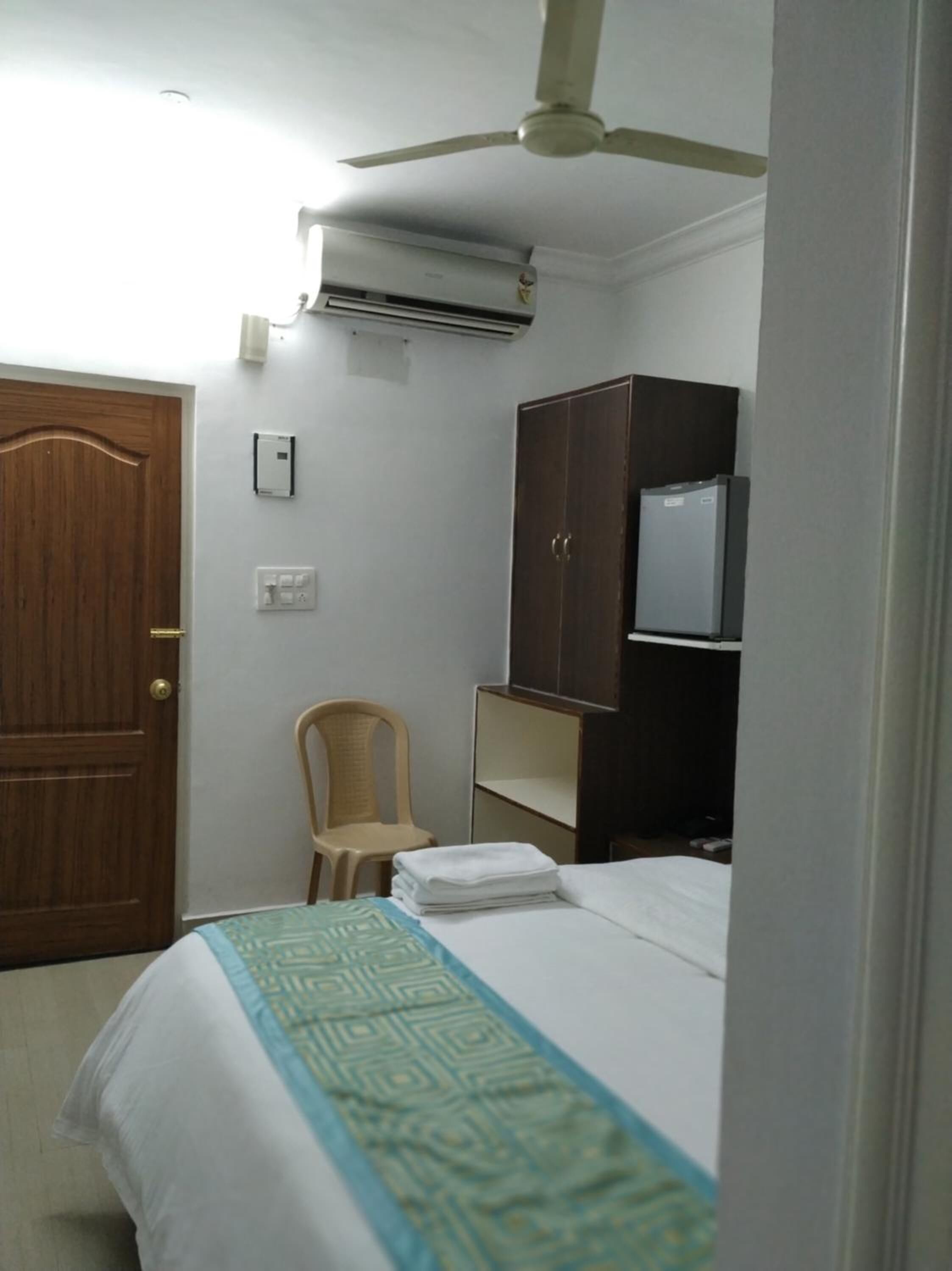 A bedroom with a bed, a wardrobe, a chair, a ceiling fan, and an air conditioning unit.