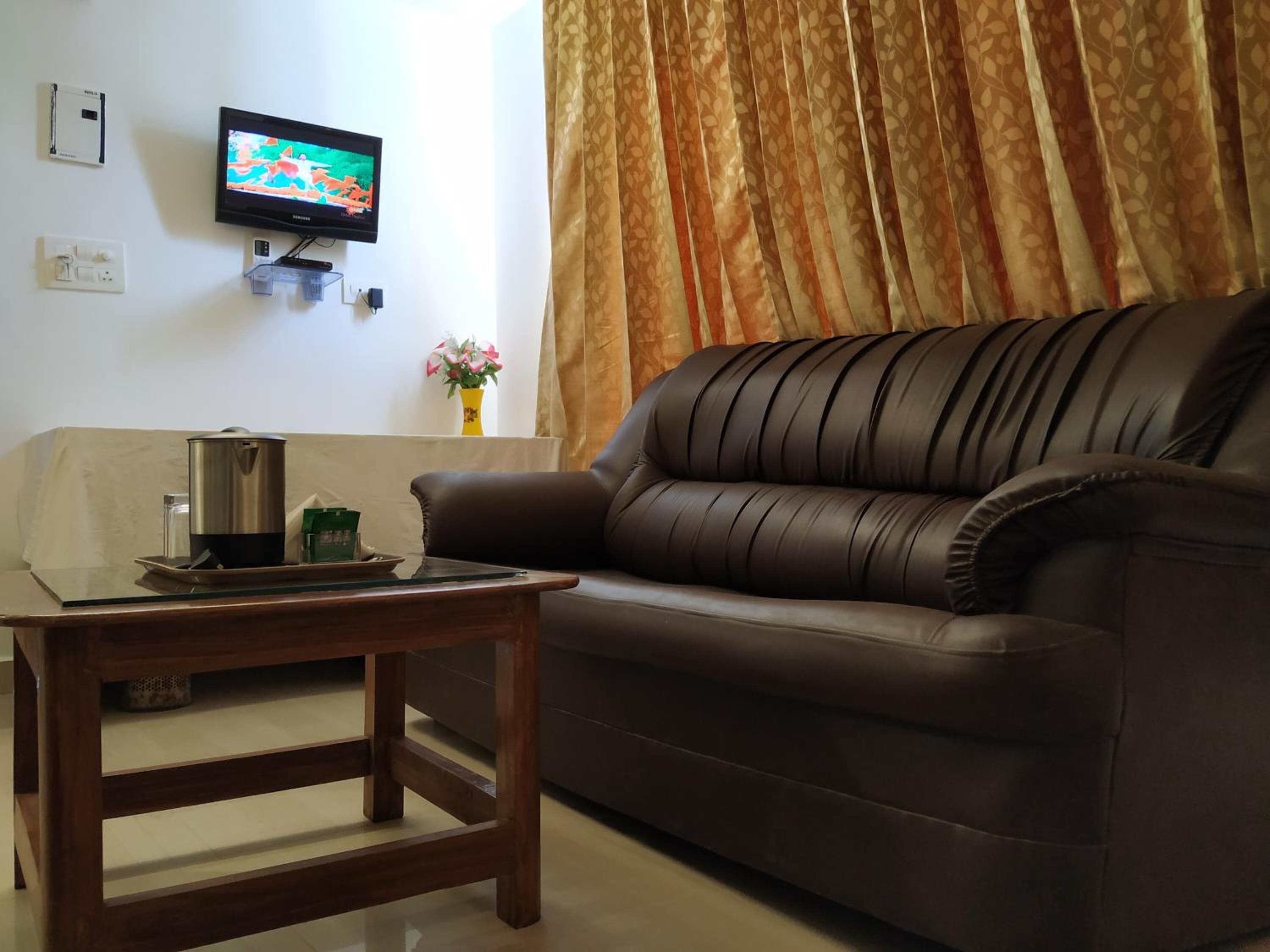 A living room with a brown leather sofa, a wooden coffee table, a television mounted on the wall, and a window with curtains.
