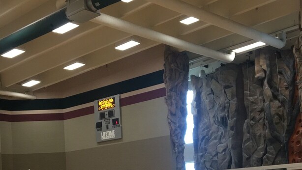 An indoor gymnasium with a wooden floor, climbing wall, and a scoreboard. - MUST STAY very big space (Aurora)