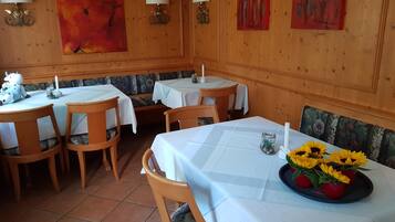 Uma sala de jantar com painéis de madeira, toalhas de mesa brancas e almofadas florais.