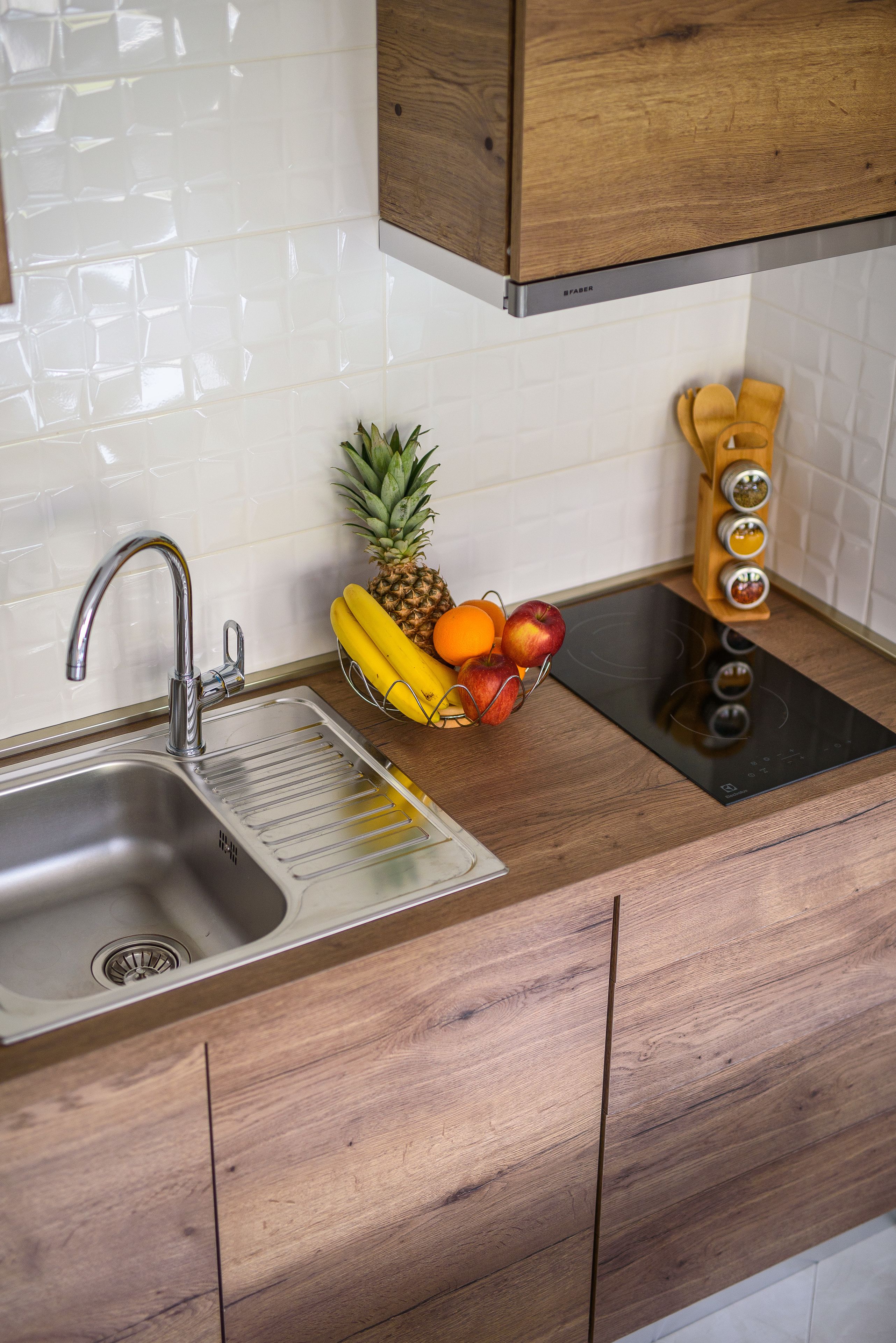 A kitchen with a stainless steel sink, wooden cabinets, a built-in stove, and a fruit bowl with bananas, apples, and oranges.