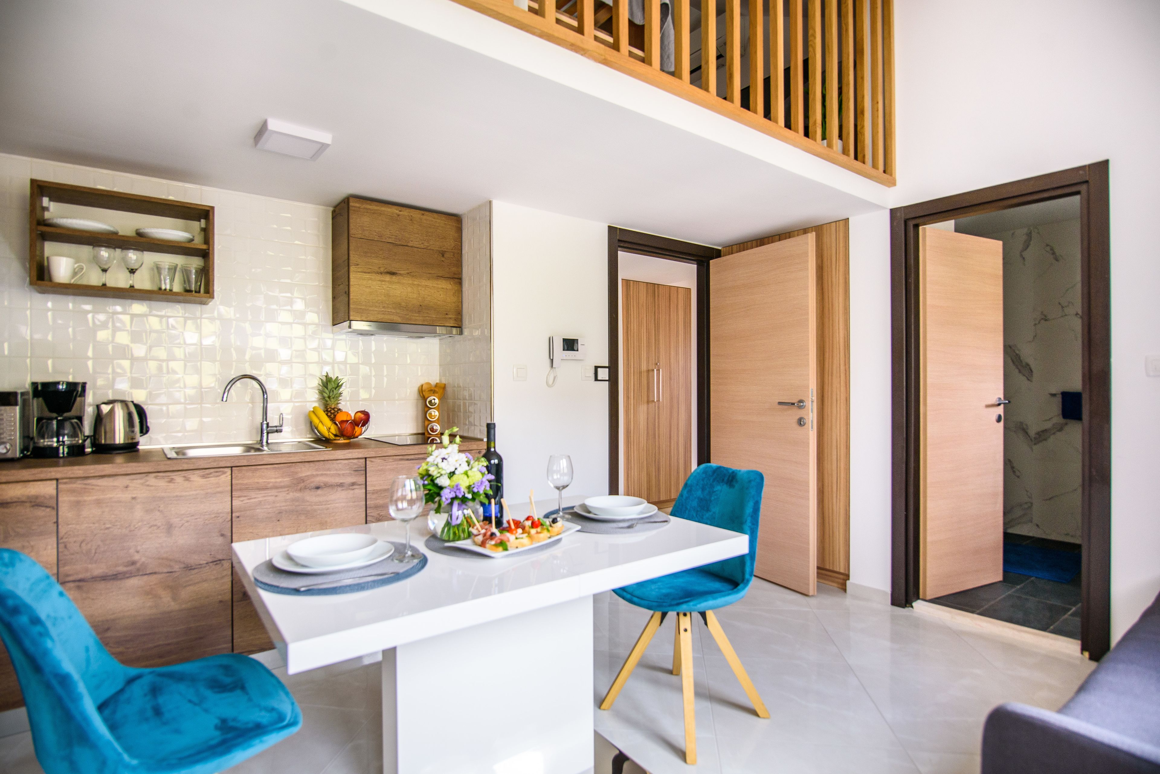 A modern kitchen with wooden cabinets, a white countertop, and a dining area with a white table and blue chairs.