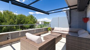 Une terrasse sur le toit, aménagée avec des meubles en osier, un pot de fleurs et offrant une vue sur les arbres et les bâtiments.