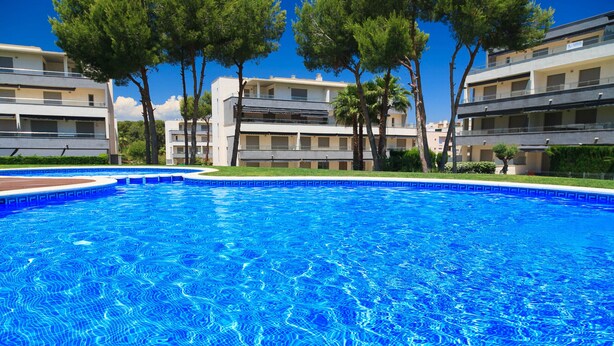 Une piscine à l’eau d’un bleu cristallin, entourée d’arbres et de bâtiments modernes.