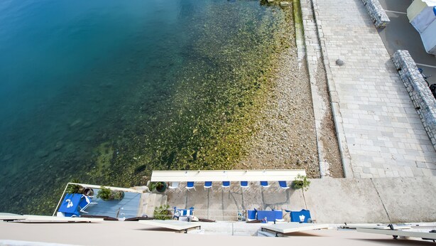 A waterfront hotel with a clear view of the sea, a stone pathway, and blue umbrellas. - Sunrise Sea view (Rovinj)