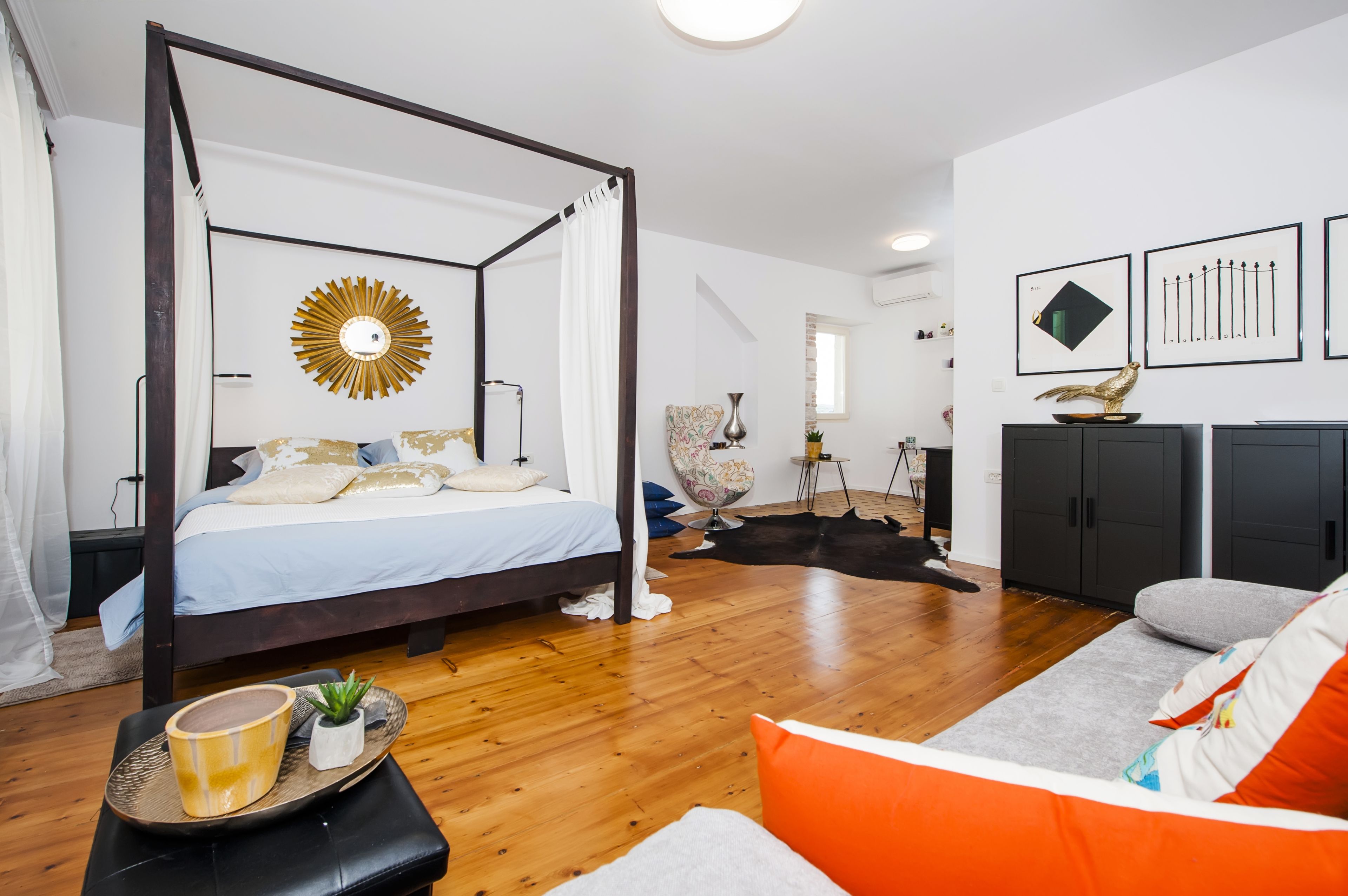 Un dormitorio con cama con dosel, un espejo grande con diseño de sol y estilo de decoración moderno.