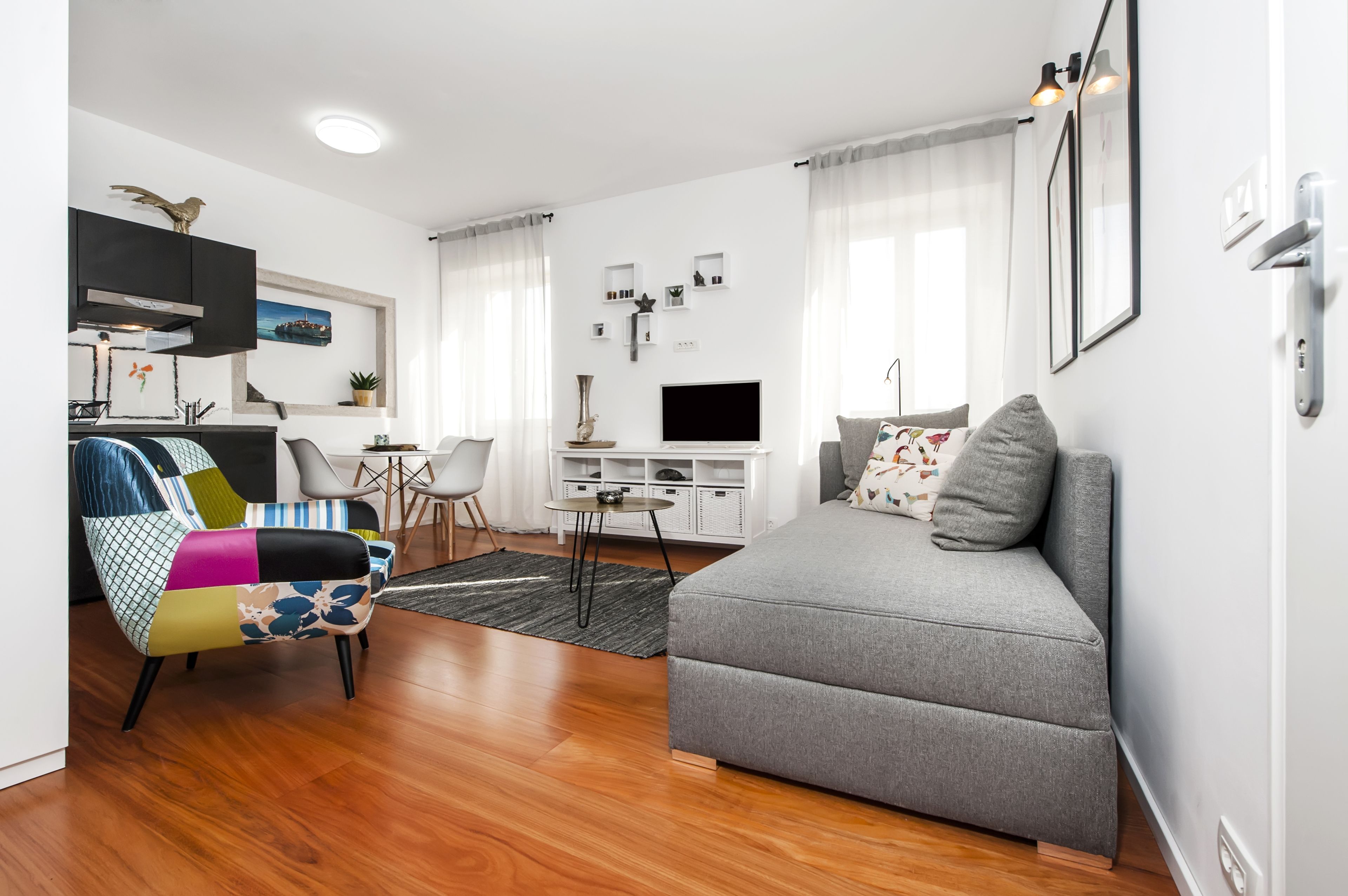A modern living room with a grey sofa, colorful armchair, and a flat-screen TV.