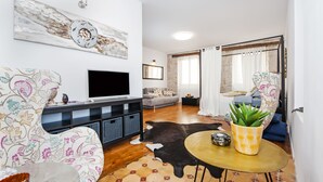 A living room with a flat-screen TV, patterned sofa, leather rug, and a small round table with a plant. - Sunrise Sea view (Rovinj)
