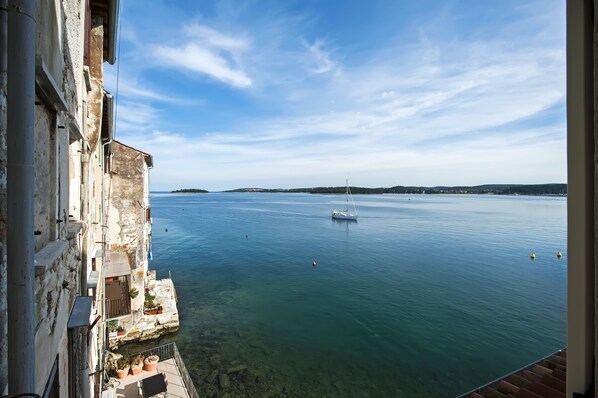 Vista des d'un balcó sobre un mar tranquil, amb un veler, aigua cristal·lina i terra a la distància.