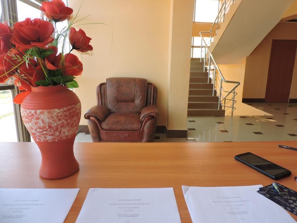 A desk with papers, a smartphone, and a vase of flowers in a modern lobby with a staircase and a leather chair.