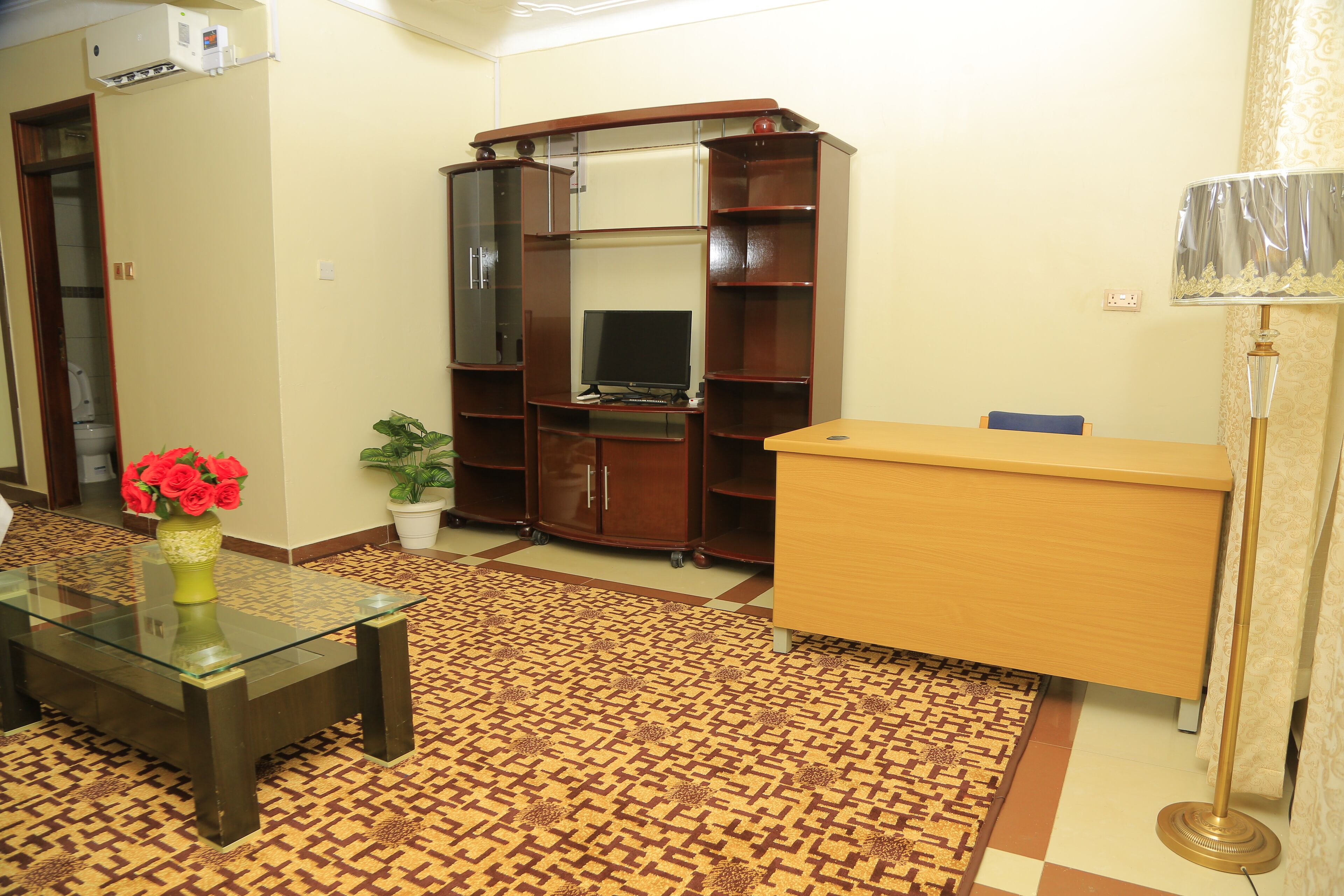 A living room with a glass coffee table, a wooden cabinet, a television, and a patterned carpet.