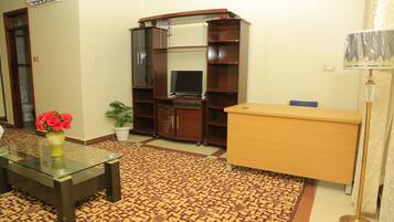 A living room with a glass coffee table, a wooden cabinet, a television, and a patterned carpet.