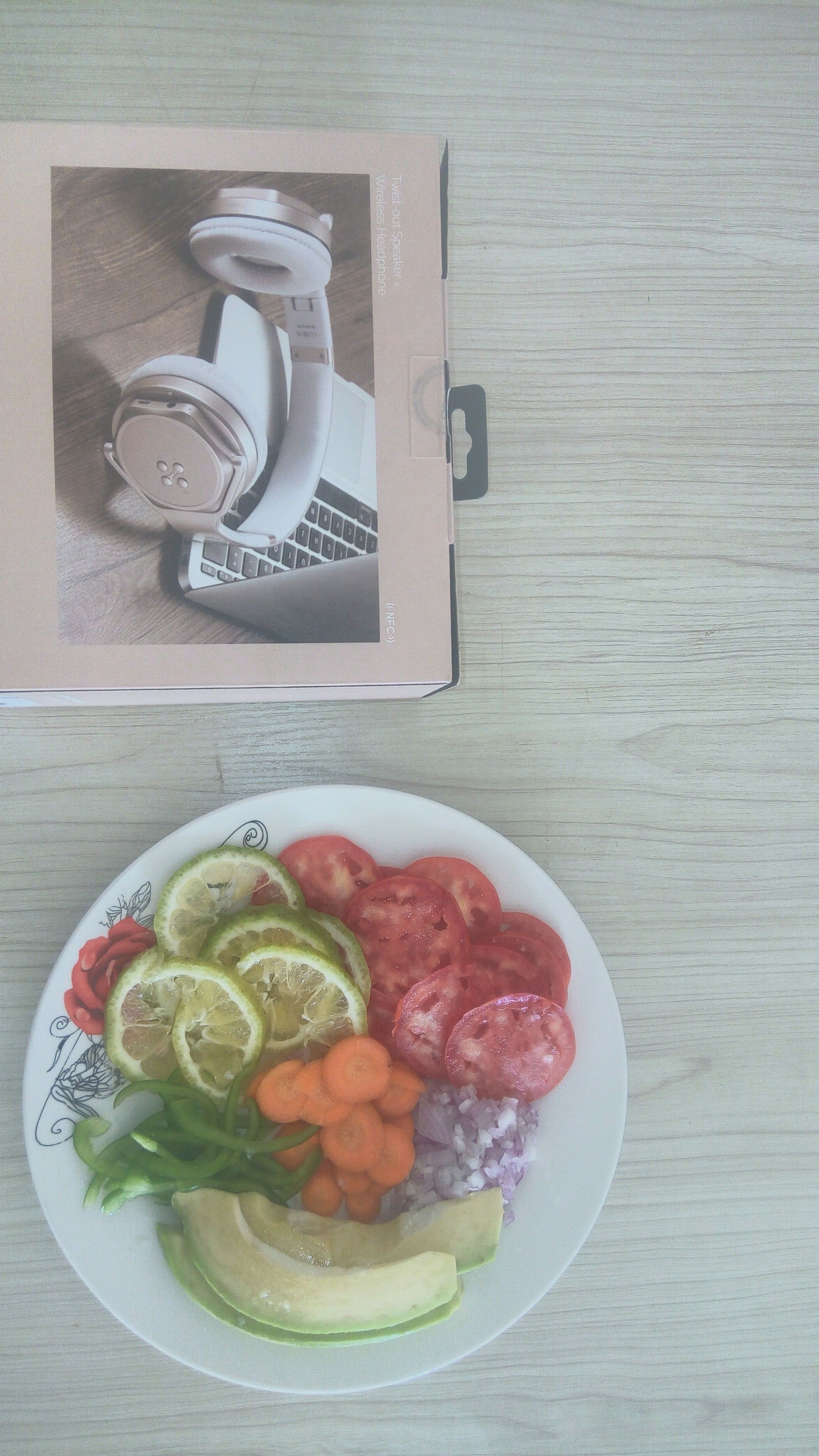 A plate of sliced vegetables and a box with a white device on a wooden surface.