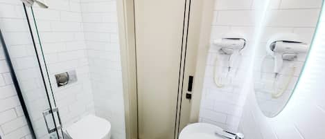 A bathroom with a toilet, a sink, a glass shower enclosure, and two hair dryers mounted on the wall.