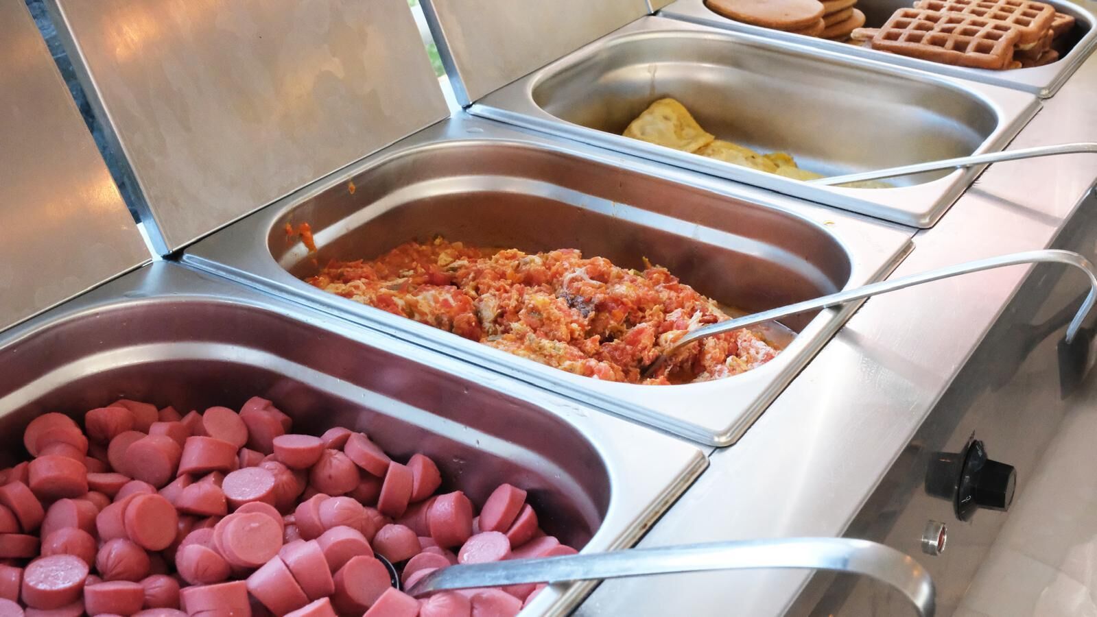 A buffet with various food items including sausages, a tomato-based dish, and waffles.
